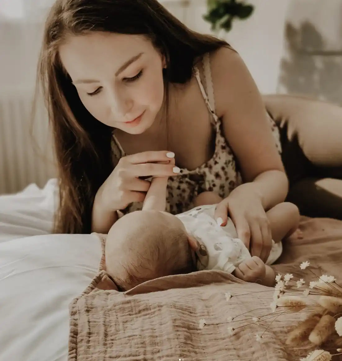 Eine Mutter hält zärtlich die Hand ihres Babys, während sie auf einem Bett liegt.