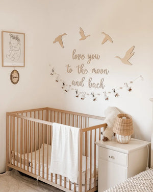 Licht holz kinderbett mit senkrechten stegen und weißer decke neben süße personalisierte holztafel im vintagestil